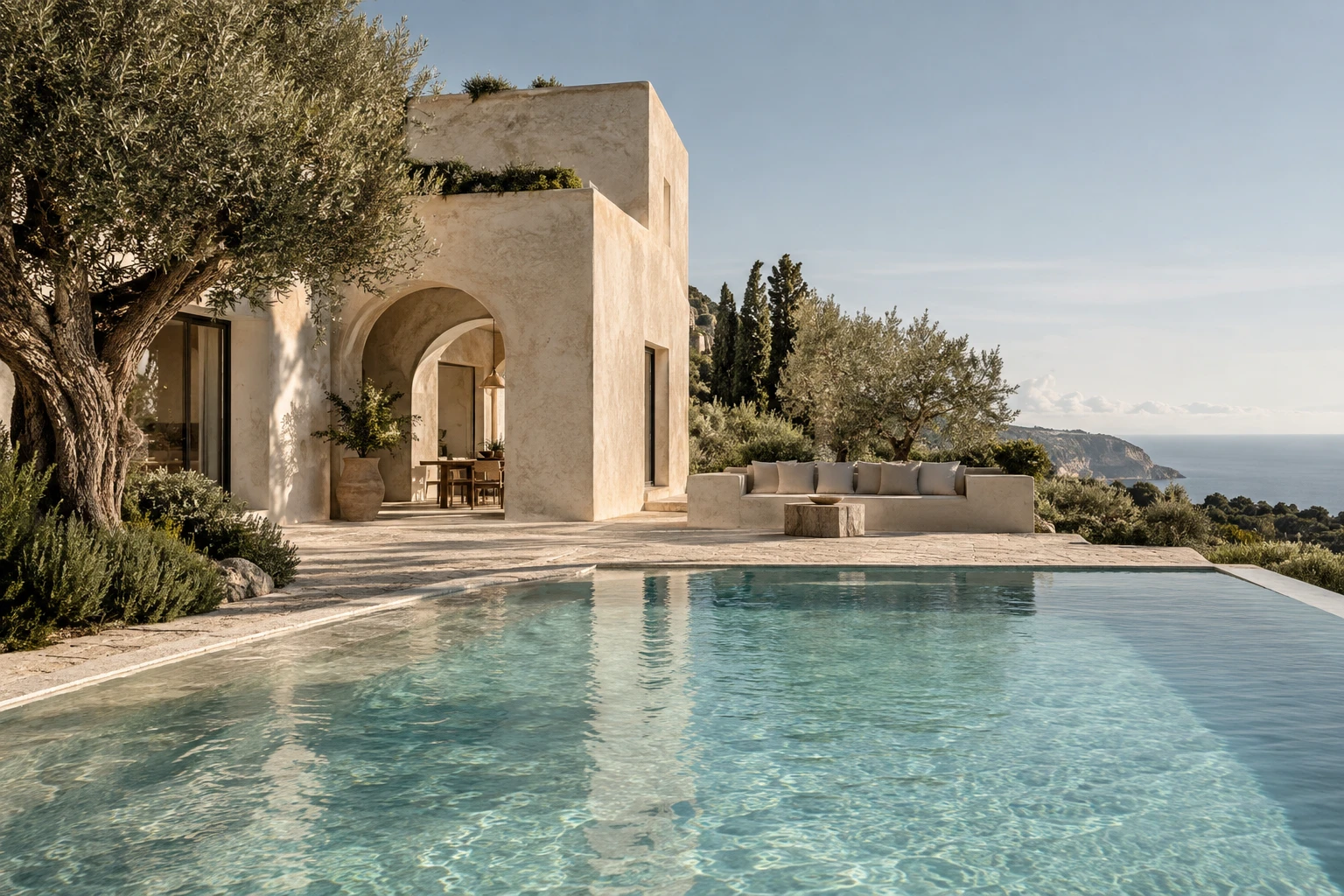 Limewashed Mediterranean villa with an arched terrace, olive tree and a sea-view pool